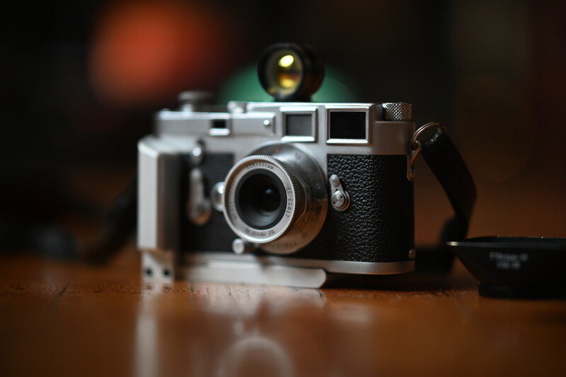 Vintage rangefinder camera with textured black body and chrome accents on wooden surface.