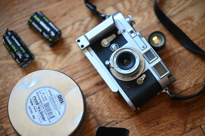 Vintage rangefinder camera with film rolls and accessories arranged on wooden surface.