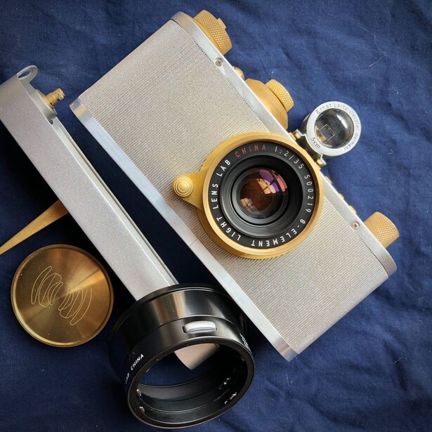 Vintage rangefinder camera with cream and brass finish displayed with accessories on blue fabric.