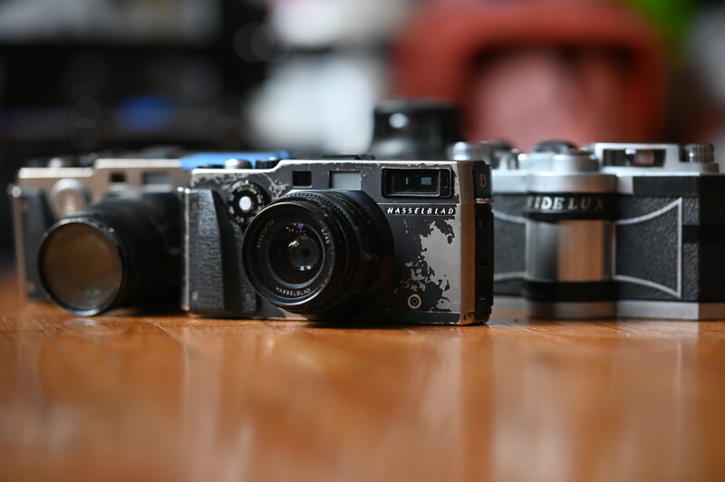 Three vintage rangefinder cameras arranged in a row on a wooden surface with blurred background.