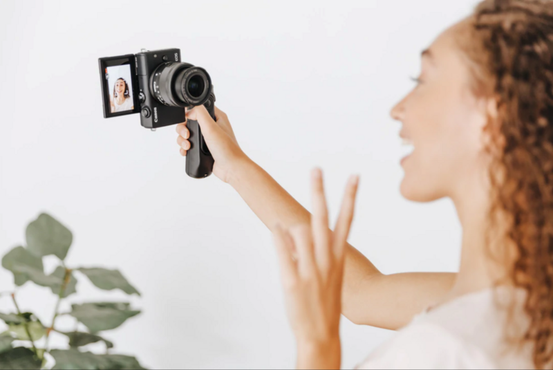 Woman holding vintage film camera up to her eye while operating the manual focus and controls.