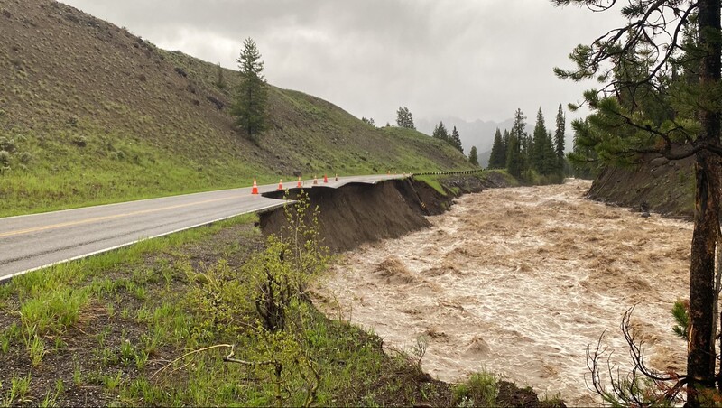 Swollen river with turbid water rushing alongside a damaged highway during flood conditions.
