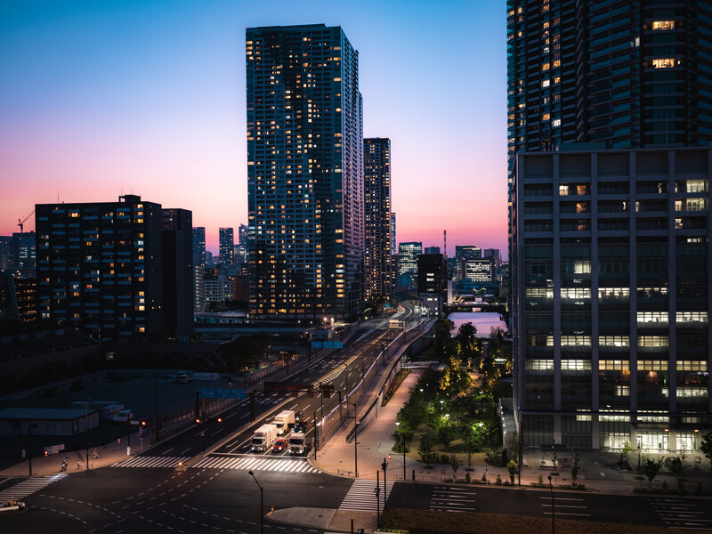Urban cityscape at twilight with illuminated high-rise buildings and light trails from traffic below.