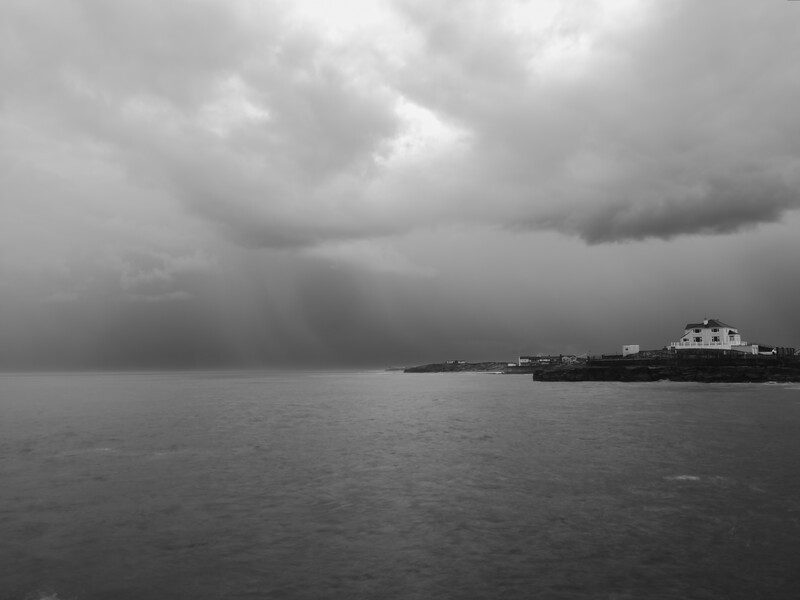 Industrial cargo ship anchored in calm water beneath dramatic storm clouds.