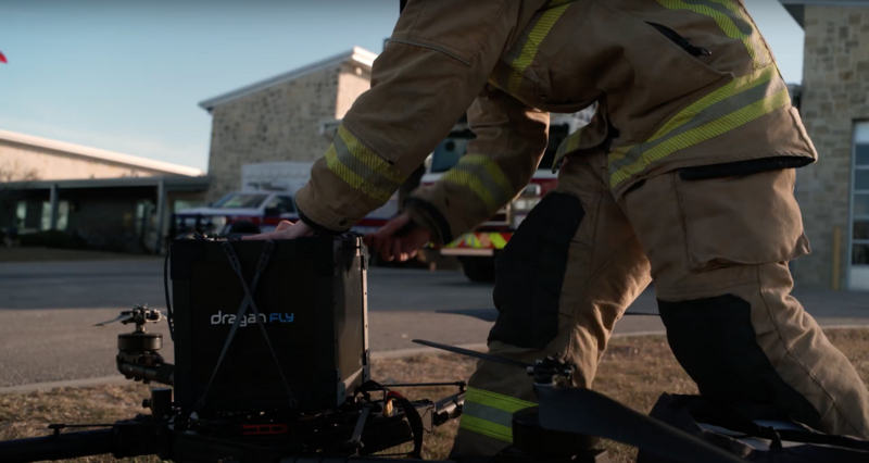 Firefighters in turnout gear operating rescue equipment on pavement near a station building.