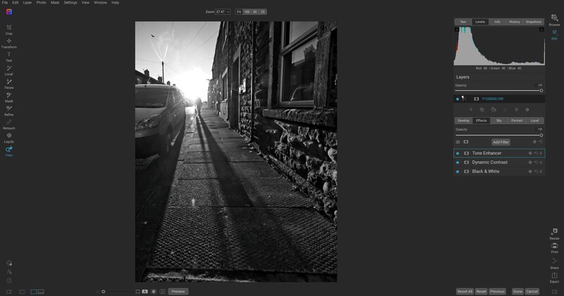 Narrow urban street lined with buildings and graffiti, strong sunlight creating dramatic shadows on cobblestone pavement.