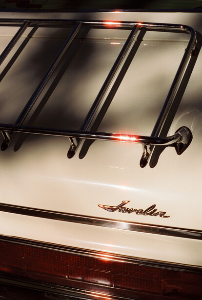 Chrome roof rack with diagonal straps on a classic car hood with script badging.