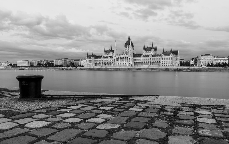 Gothic parliament building with spires reflected in calm river, viewed from textured foreground.