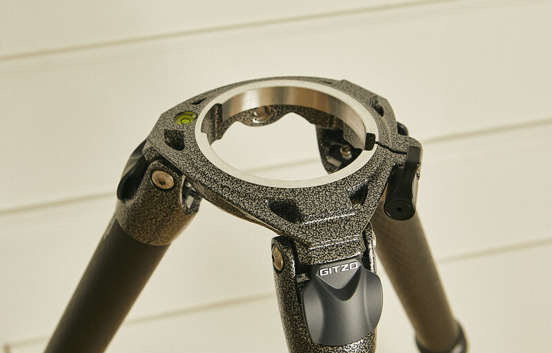 Close-up of a tripod head with textured gray finish and black components, viewed from above against a white background.