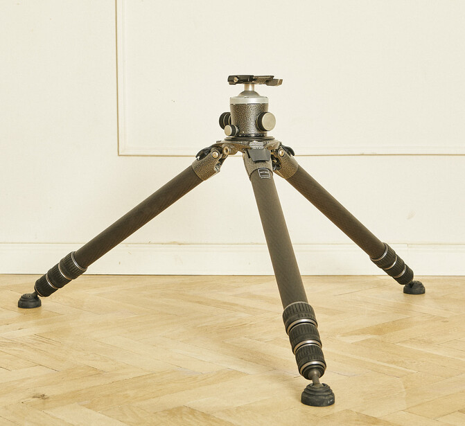 Heavy-duty tripod with ball head and extended legs on wooden floor against white wall.