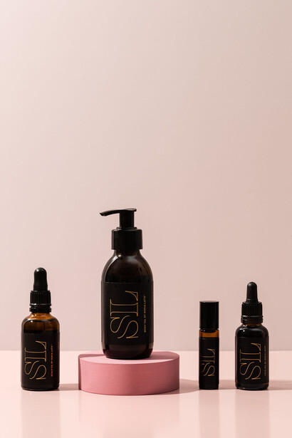 Luxury skincare bottles arranged on a pink cylindrical pedestal against a neutral beige background.