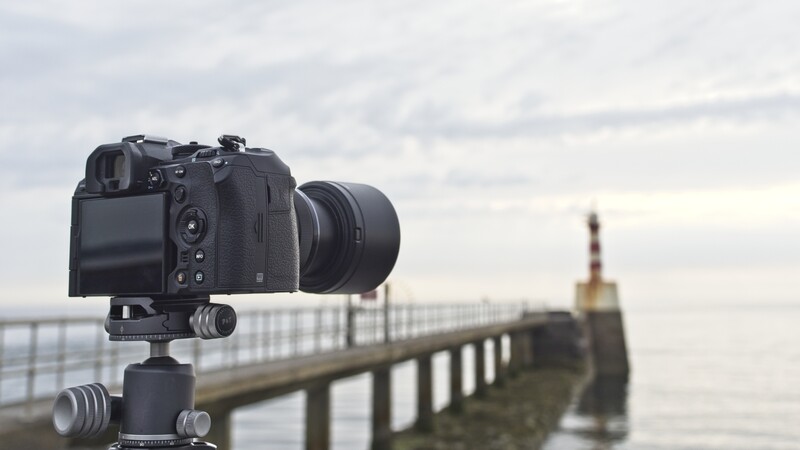 DSLR camera mounted on tripod with telephoto lens pointed at pier extending into sea.
