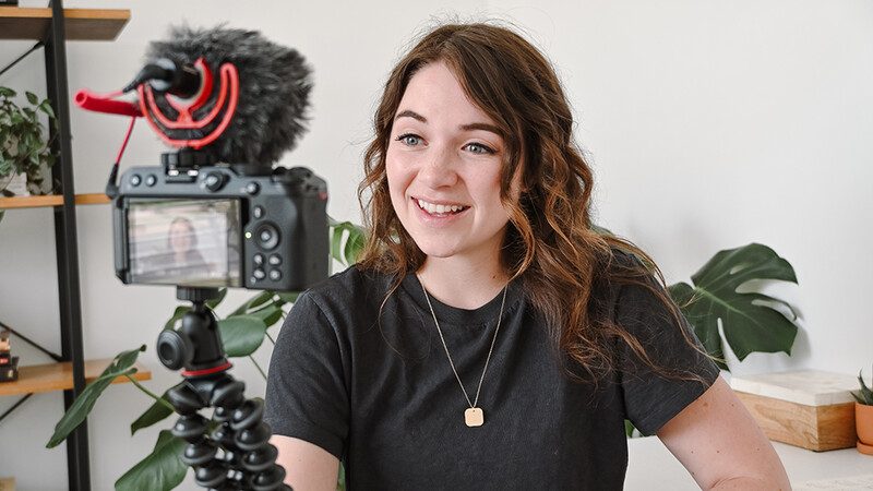 Content creator at desk with professional video camera on tripod and directional microphone setup.