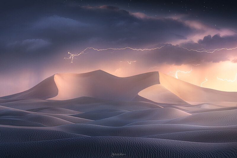 Desert sand dunes silhouetted against a dramatic sky with lightning and warm golden light at sunset.