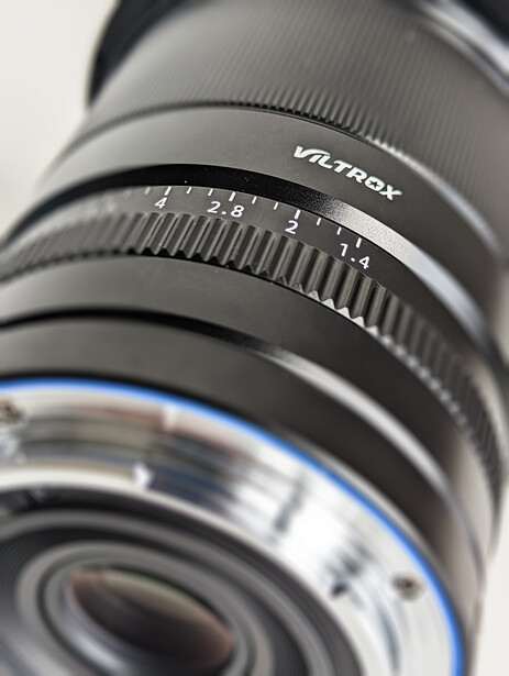 Close-up of a camera lens showing focus ring, depth of field markings, and blue lens coatings.