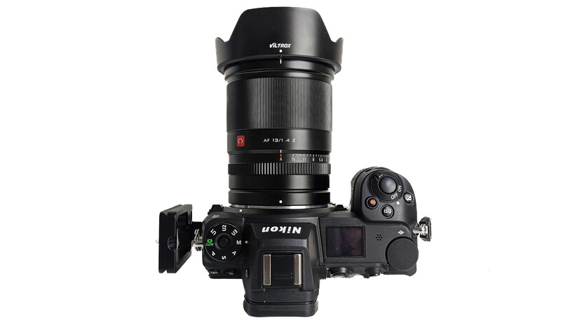 Mirrorless camera with fast telephoto lens and hood mounted on top, viewed from above against white background.