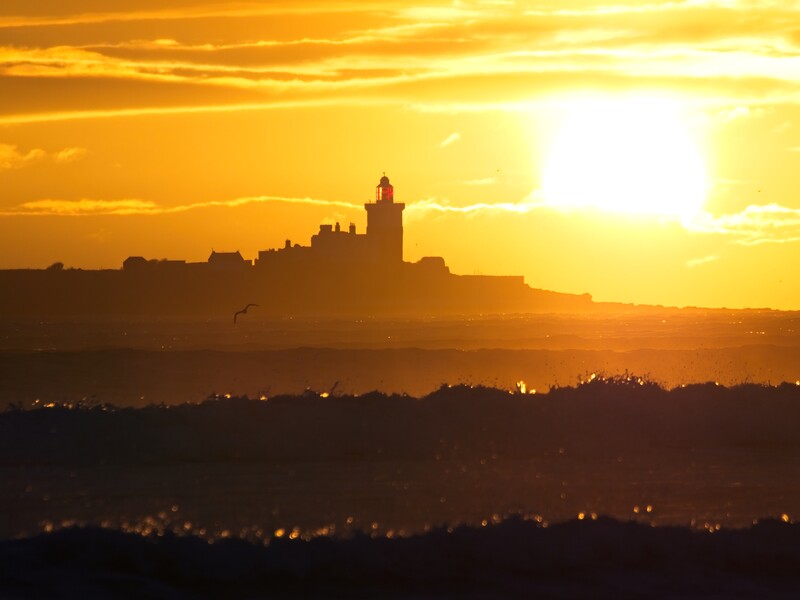 Silhouetted cityscape with prominent tower structure against golden sunset sky.
