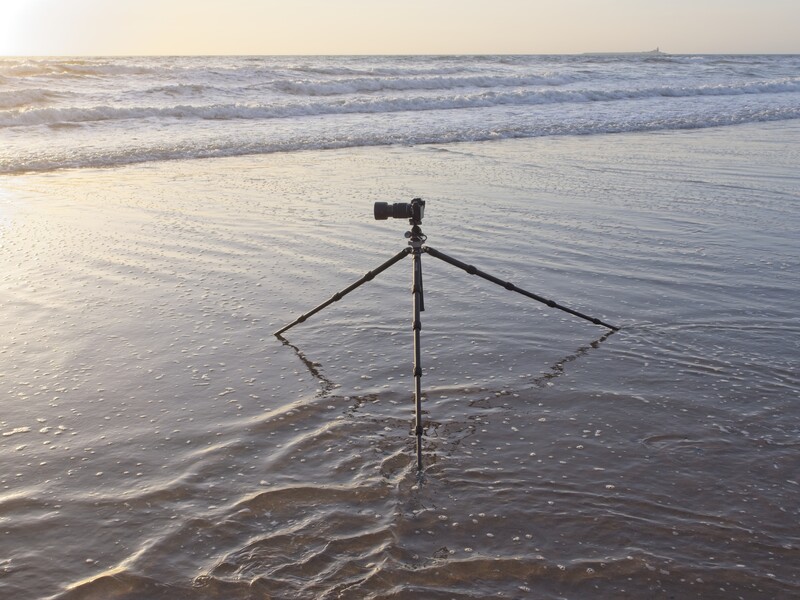 Camera on tripod positioned in shallow ocean water at sunset or sunrise.