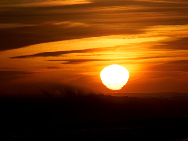 Large sun at horizon during golden hour with dramatic orange and amber sky gradating to dark silhouettes below.