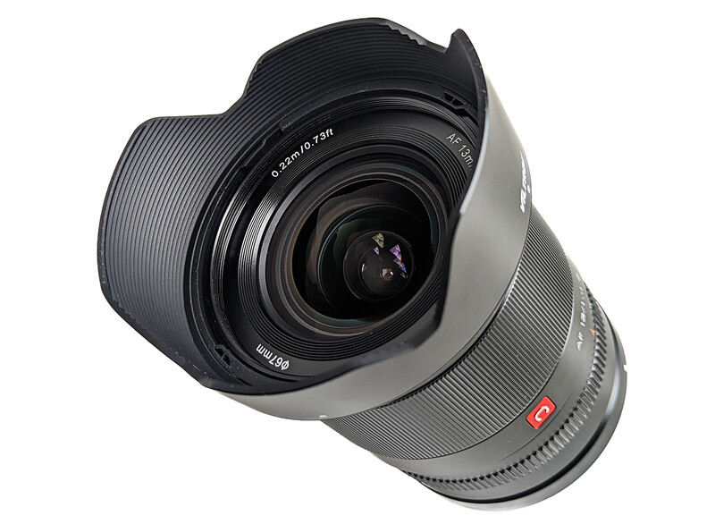 Wide-angle camera lens with gray and black barrel, hood, and glass elements visible against white background.