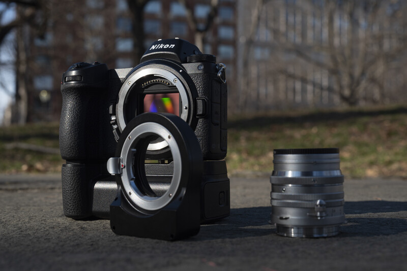 Nikon DSLR camera with battery grip and interchangeable lens displayed on pavement outdoors.