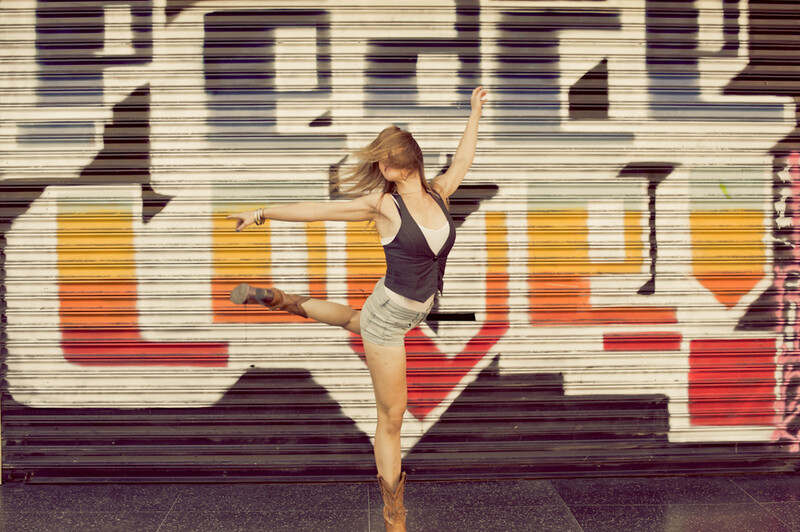Dancer performing an arabesque pose against a colorful geometric mural backdrop.