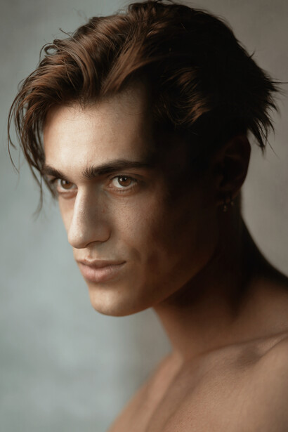 Male model with styled brown hair in three-quarter view against neutral background.