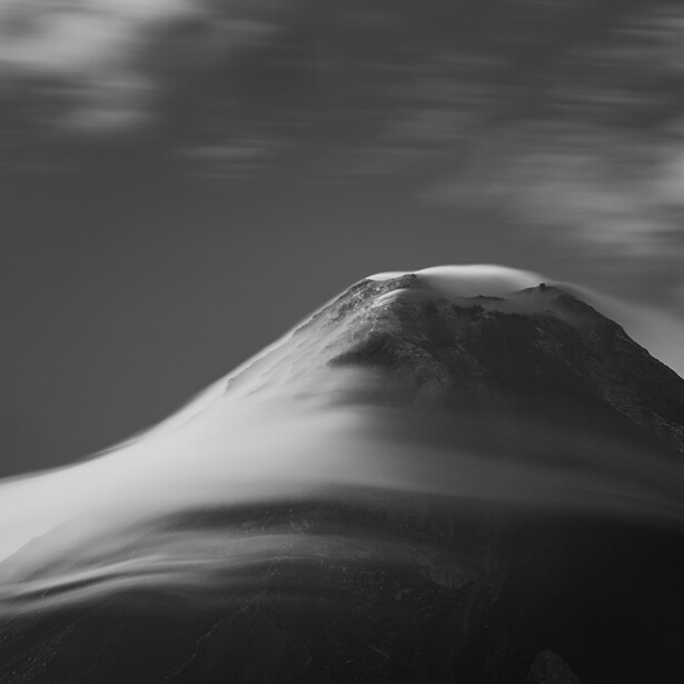 Snow-covered mountain peak in monochrome against a dramatic clouded sky.