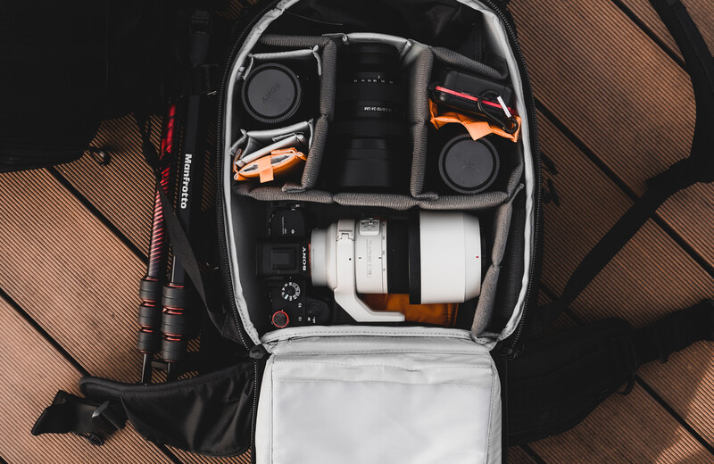 Overhead view of an organized camera backpack with compartments holding lenses, camera body, cables, and accessories.