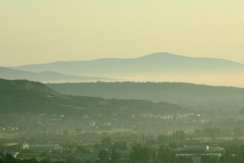 Layered mountain landscape with misty valleys and a town nestled in the foreground under hazy morning light.