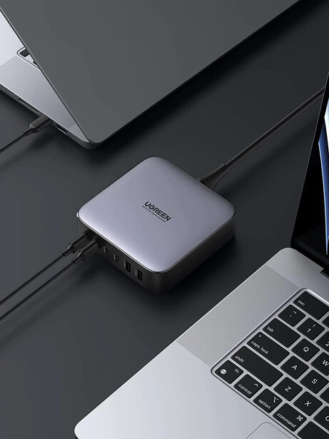 Compact external SSD storage device positioned between a laptop keyboard and closed laptop on a dark gray desk surface.