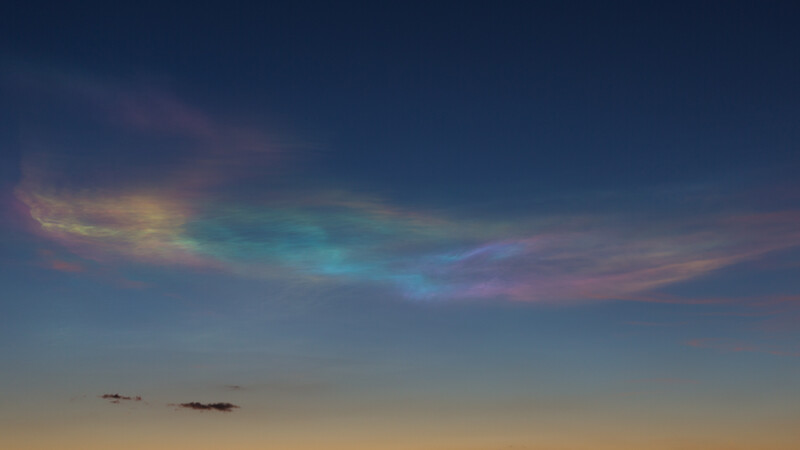 Iridescent cloud formation during twilight with golden and turquoise hues against a deep blue sky.