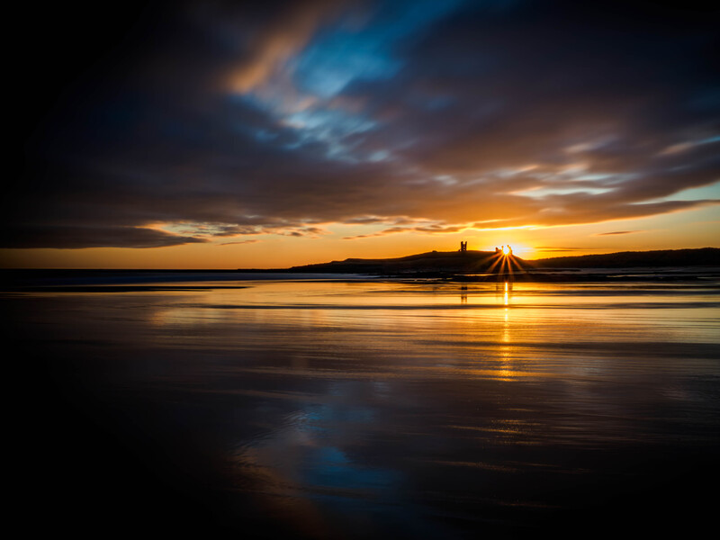 Golden sunset over a wet beach with dramatic clouds reflected in the sand.