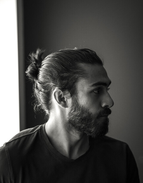 Black and white profile portrait of a man with a full beard and long hair pulled back.