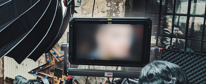 Production monitor displaying a washed-out video feed mounted on a camera rig beside lighting equipment.
