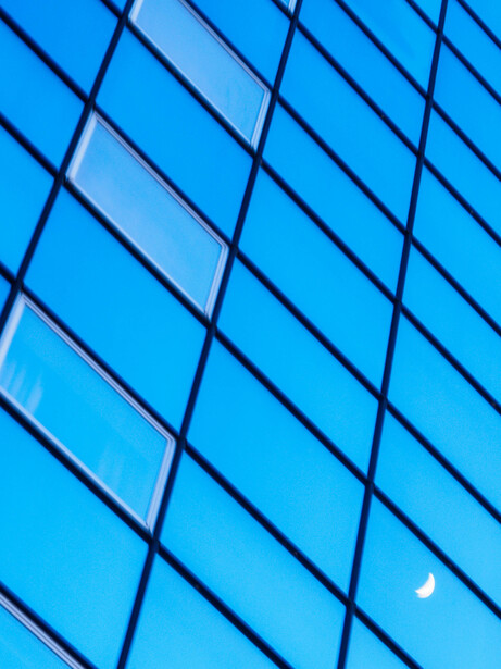 Geometric pattern of blue glass panels on a modern building facade with dark grid lines and sky reflection.