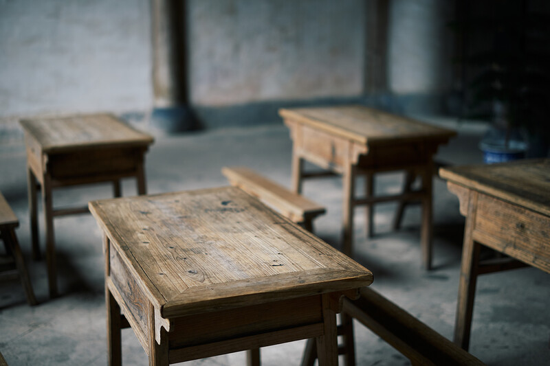 Wooden desks arranged in an empty classroom with shallow depth of field focusing on foreground table.