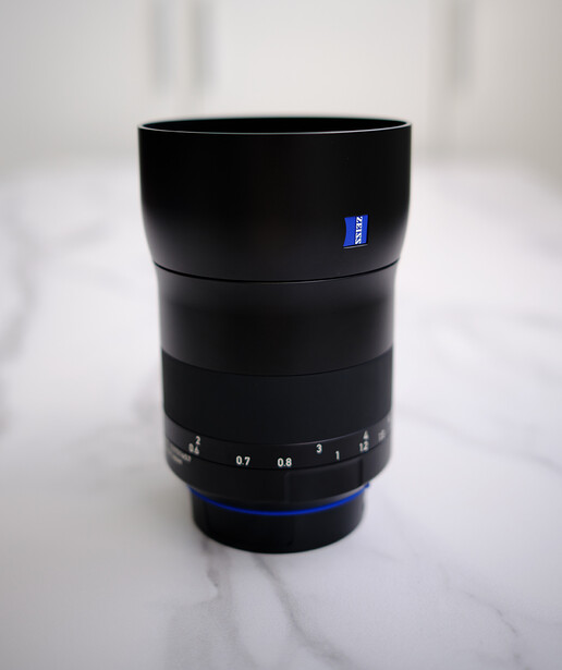 Black telephoto lens with blue accent ring and aperture scale markings, displayed against white background.