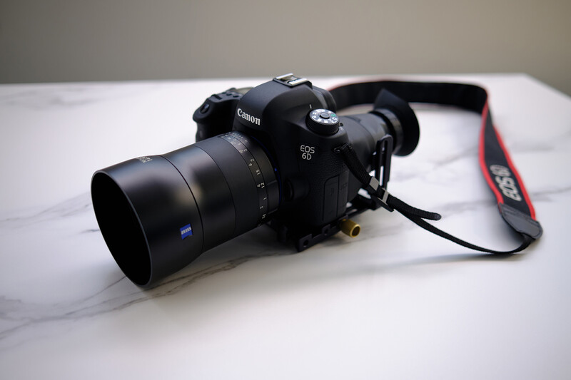 Canon EOS 6D DSLR camera with Zeiss lens on white marble surface with red camera strap.
