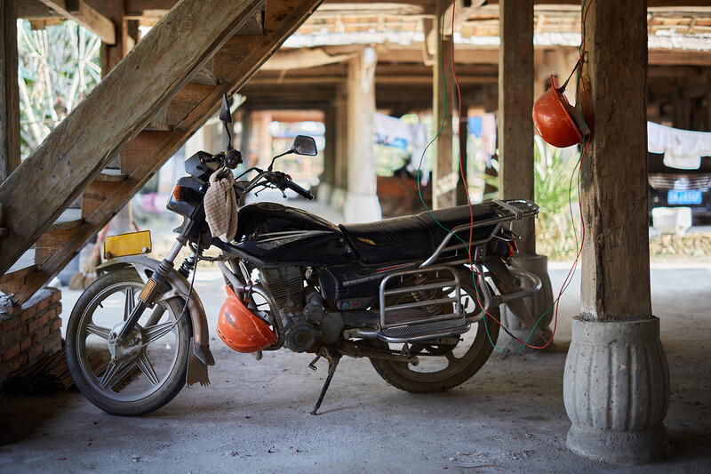 Black motorcycle parked under wooden structure with red helmet hanging on post.