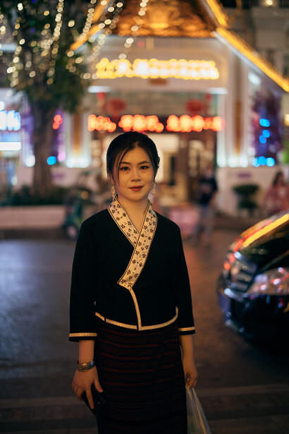 Woman in black blazer with patterned scarf standing on illuminated city street at night.