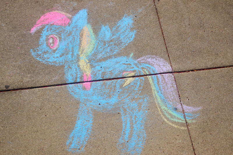 Chalk drawing of a blue pony with pink mane and yellow tail on concrete sidewalk.