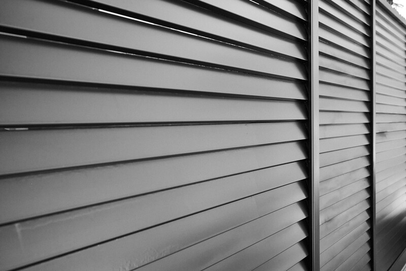 Black and white close-up of horizontal slatted panels with strong linear shadows creating depth.