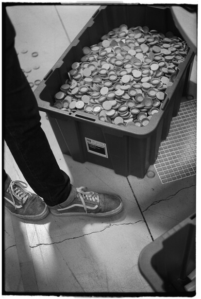 Overhead view of a container filled with coins next to a person's sneaker-clad feet.