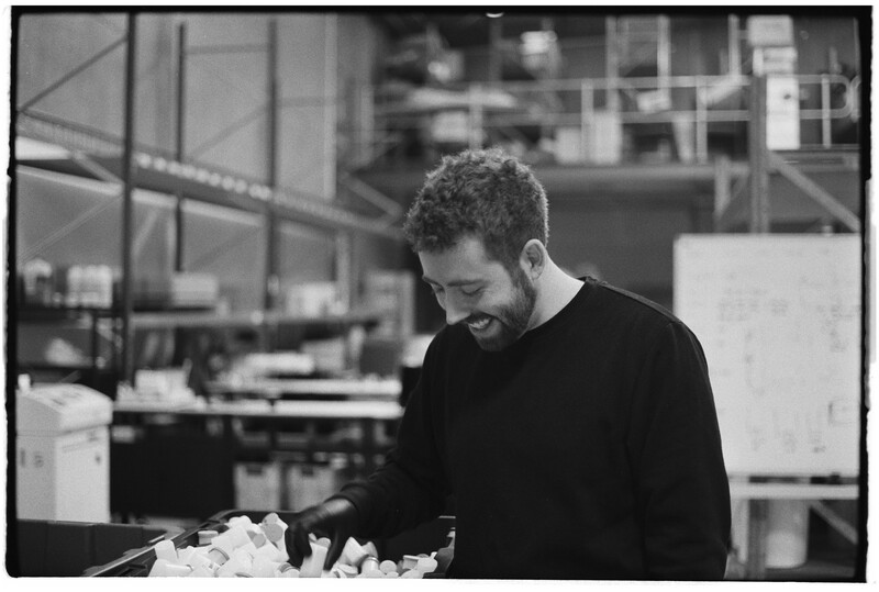 Man in black sweater examining architectural models or materials at a workspace table.