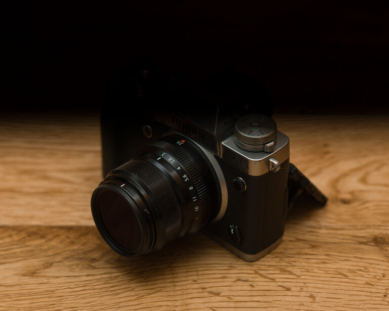 Vintage rangefinder camera with mounted lens on wooden surface, lit by warm studio lighting.