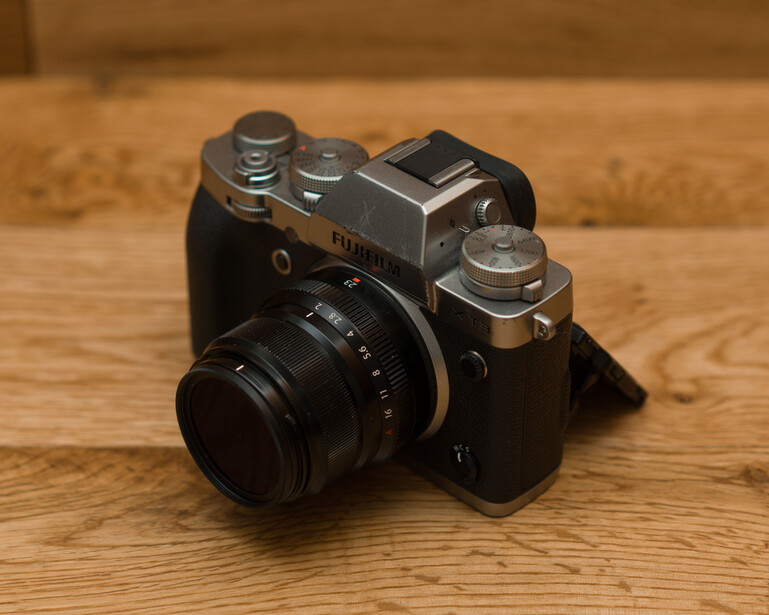 Vintage rangefinder camera with black body and chrome top plate on wooden surface.