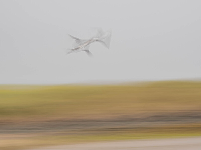 A small aircraft in flight above a blurred landscape with horizontal motion blur effect.