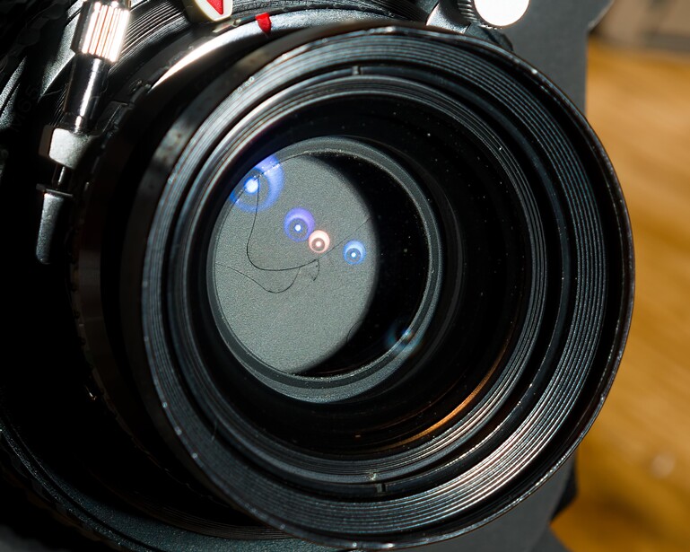 Close-up of a camera lens front element showing internal reflections and optical glass surfaces.
