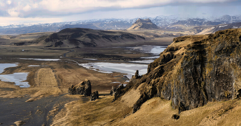 Dramatic volcanic landscape with steep basalt cliffs overlooking glacial valleys and snow-capped mountains.